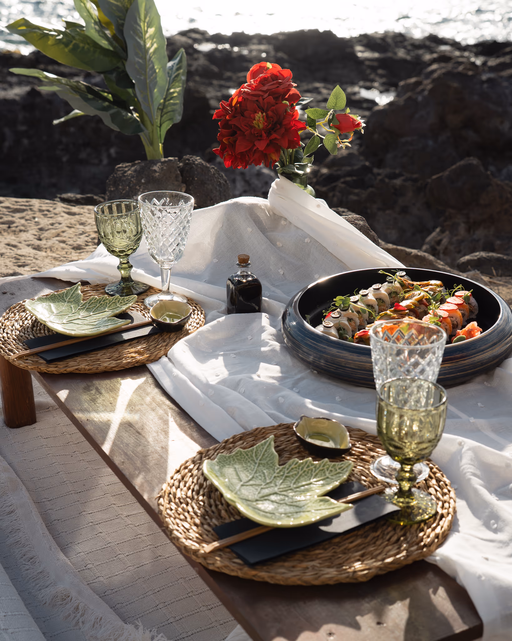 Mesa de pícnic romántico montada en una playa del sur de Tenerife, con flores, vajilla vintage y vistas al mar